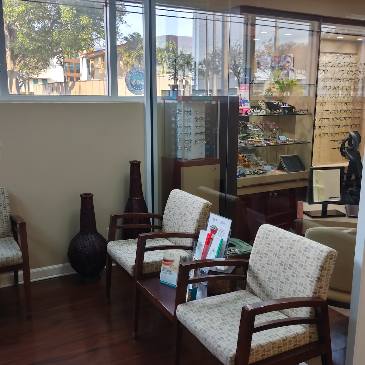 The image shows an interior view of an optician s shop with chairs arranged for customers to sit while waiting, and a display case containing eyeglasses.