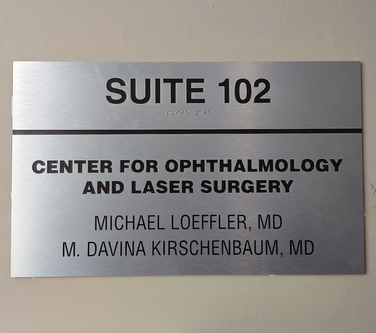 The image shows a sign for Suite 102 at an optometry and laser surgery center. It includes names, presumably staff members, and is mounted on a wall.