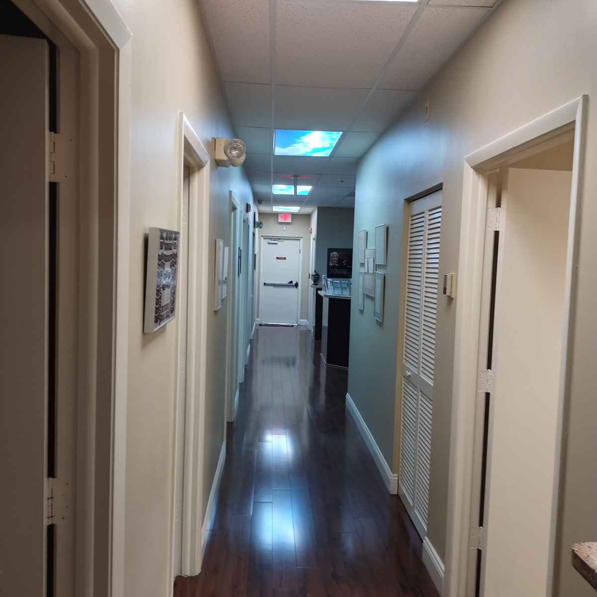 The image shows an interior hallway with a shiny floor reflecting lights, walls painted in light colors, and a row of closed doors on one side.
