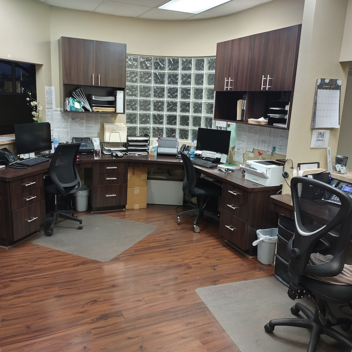 Office space with multiple desks, chairs, computers, and office equipment.
