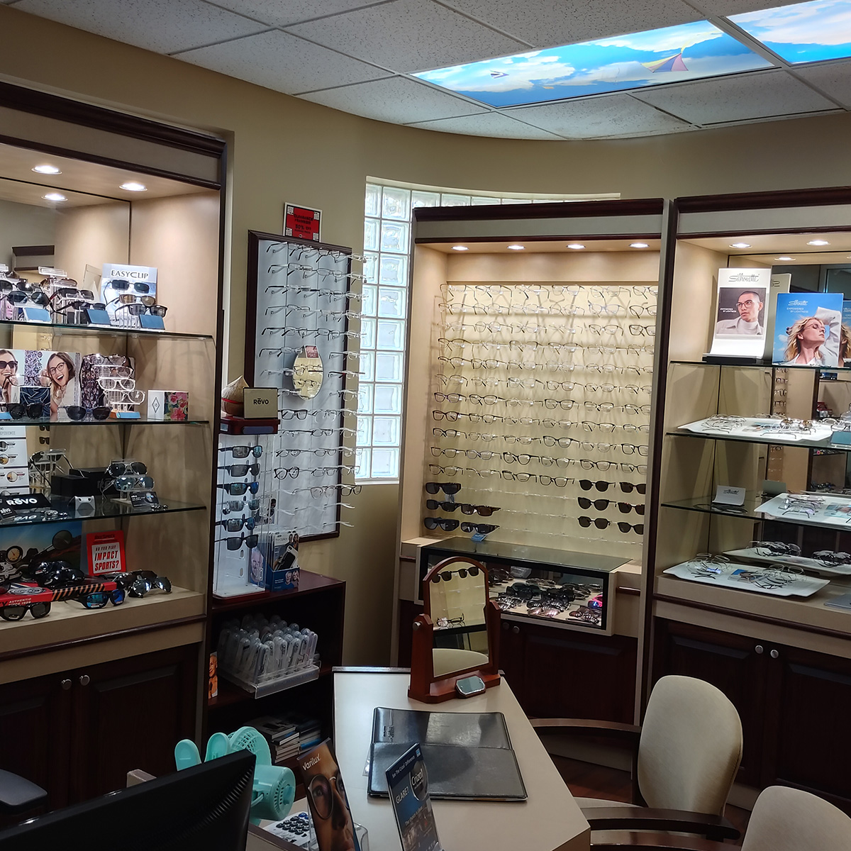 The image shows an interior view of an optician's shop with various eyewear displays and a counter area.