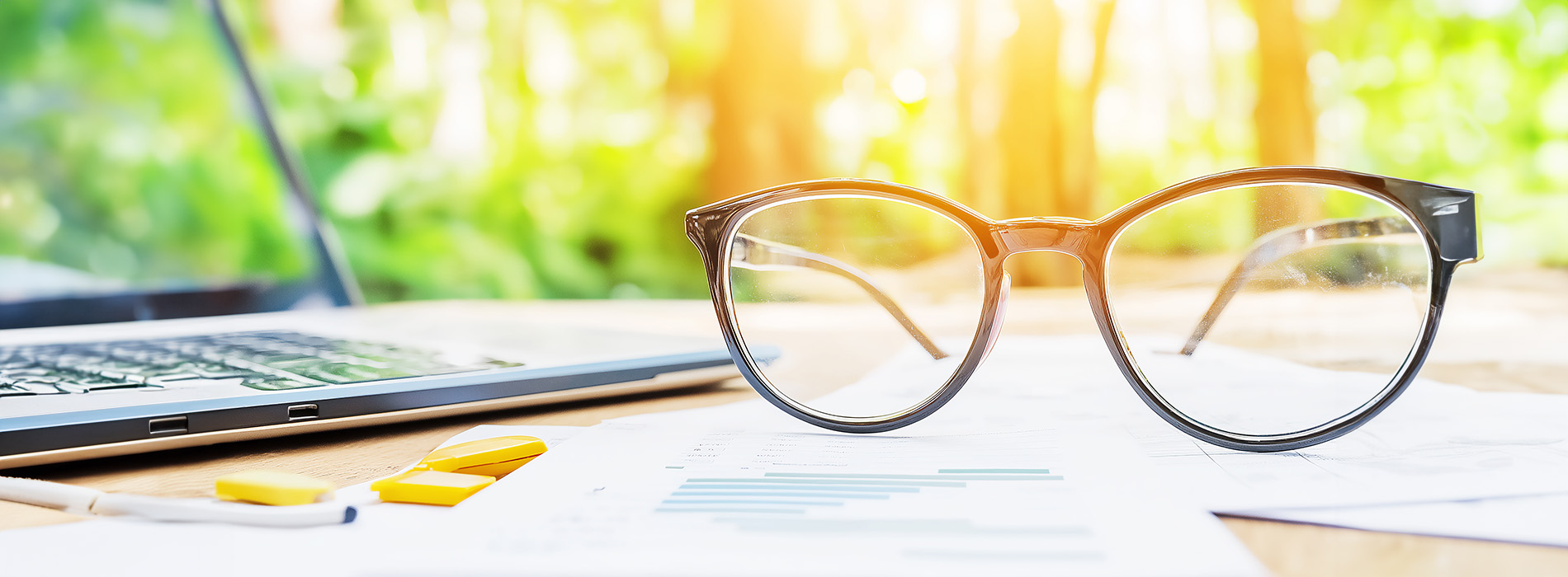 A pair of glasses on a desk with blurred background.