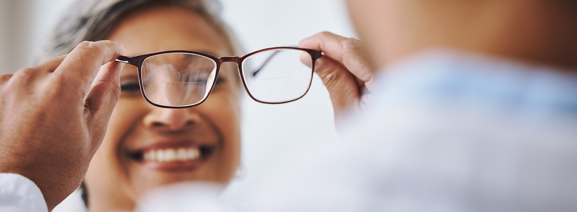 An individual holding a pair of glasses while another person looks on, both appearing to be in an optical shop setting.