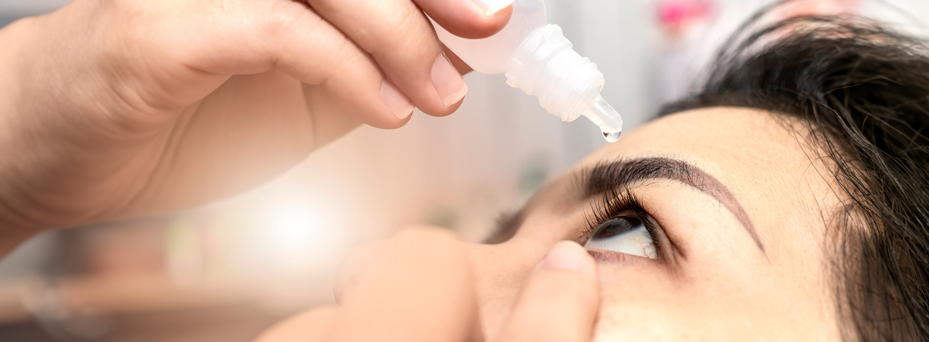 A person s hand holding an eye dropper over their face.