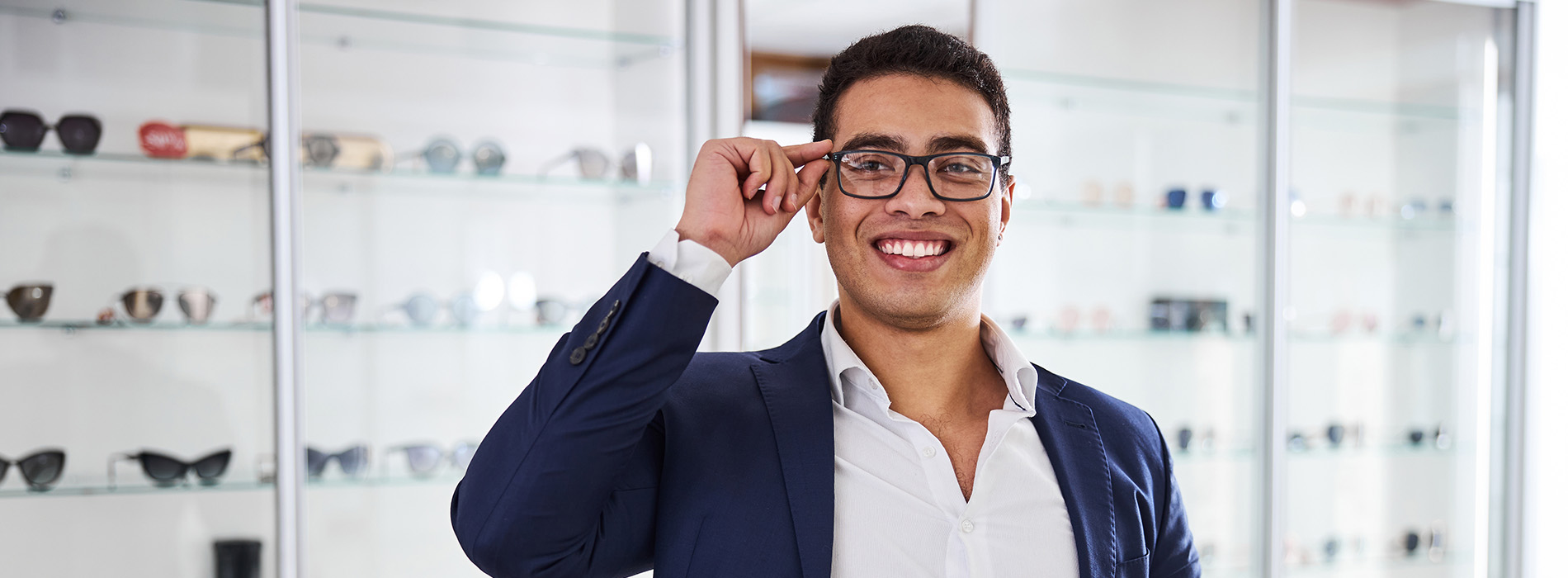 A man wearing glasses with his eyes closed is standing in front of a display case filled with eyewear.