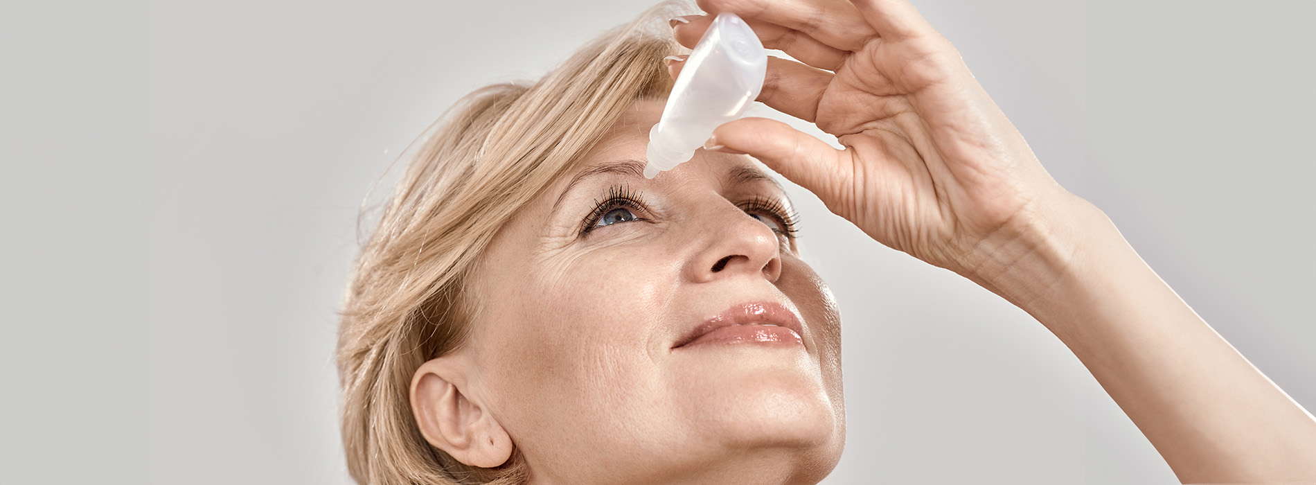 Woman applying eye drops with focus on the bottle and her eyes.