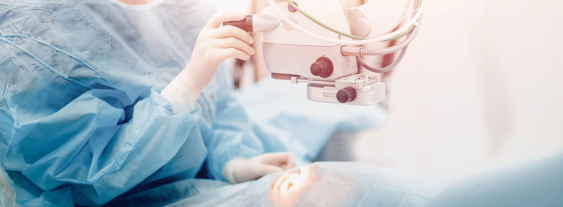 The image shows a person wearing surgical scrubs and a face mask, holding up a medical device with a screen displaying an image, likely in a hospital or medical setting.