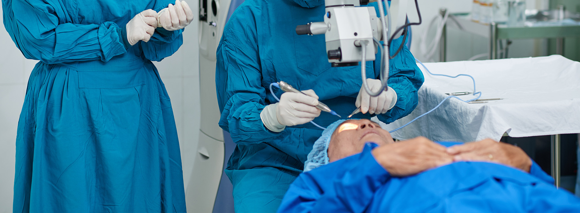 A medical professional in blue scrubs performing an eye examination on a patient using specialized equipment.