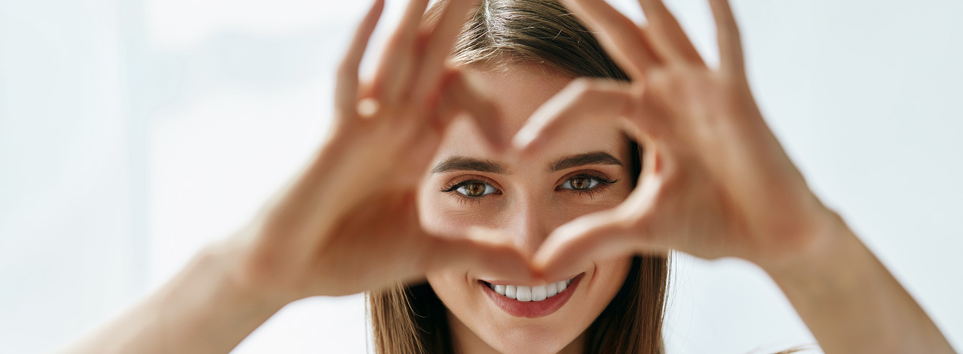 A person making a heart shape with their hands against a bright background.