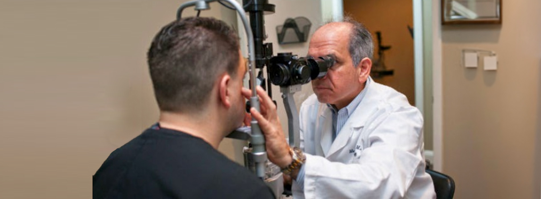 The image shows a man seated in an optometrist s chair while another person, presumably an eye doctor, examines his eyes with a device.