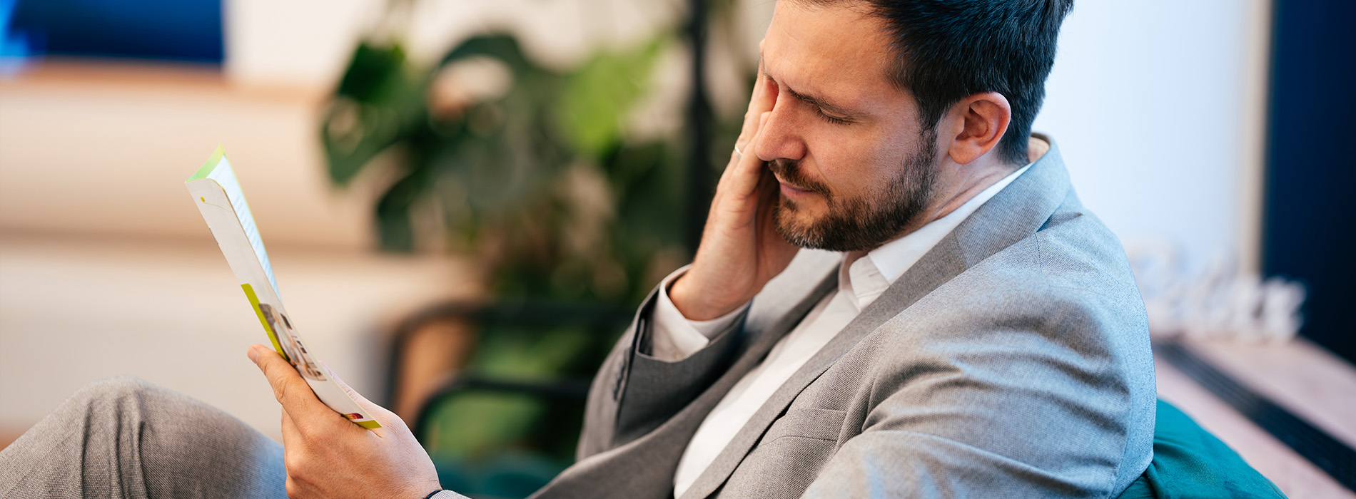 The image shows a man sitting on a chair, engrossed in reading a book.