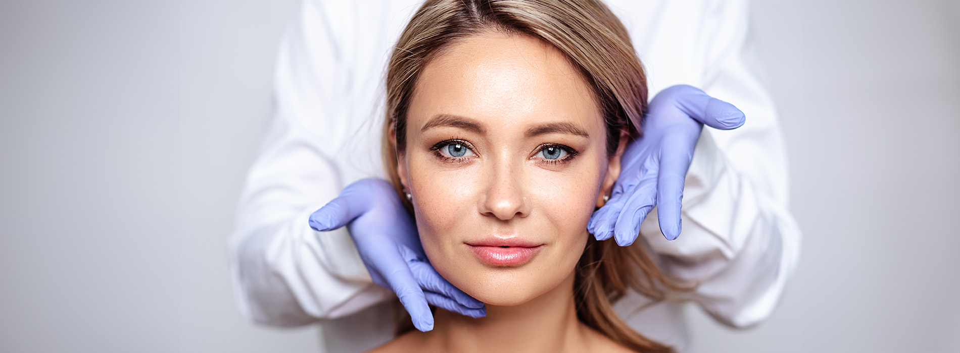 A woman receiving a facial treatment from a professional with a blue mask on her face.