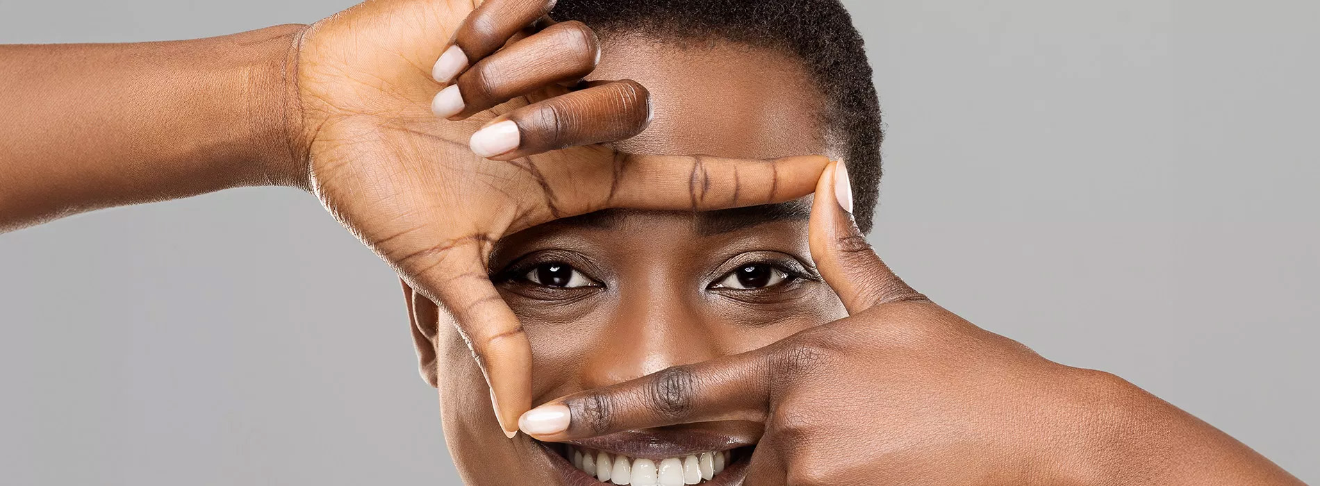 The image shows a person making a peace sign with their hands while looking through a hole, with a blurred background featuring another hand holding up a finger.