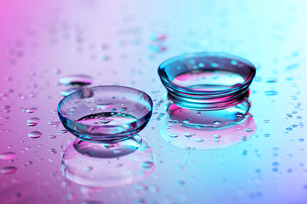 The image shows two clear glass beads resting on a surface with droplets of water around them, set against a colorful background.