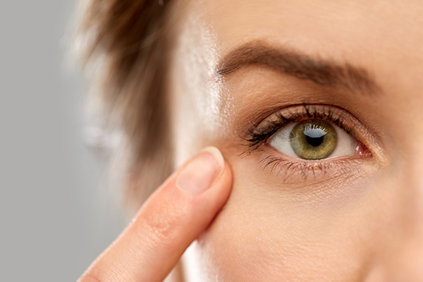 The image shows a close-up of a person s face with their eyes closed, focusing on a product or service related to skincare or beauty, such as an eye cream or treatment, indicated by the application near the eye and the magnified view of the skin.