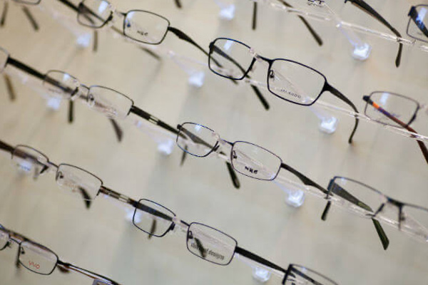 The image displays a collection of eyeglasses hanging in rows against a neutral background.