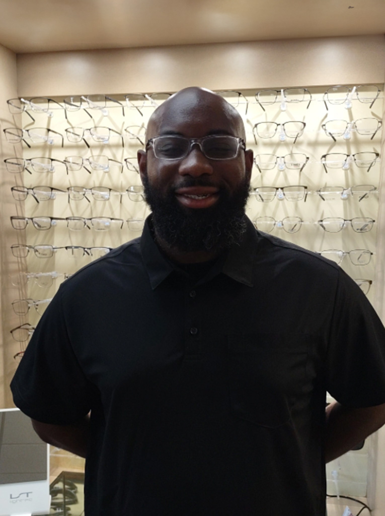 Man wearing glasses stands behind display case with eyewear.