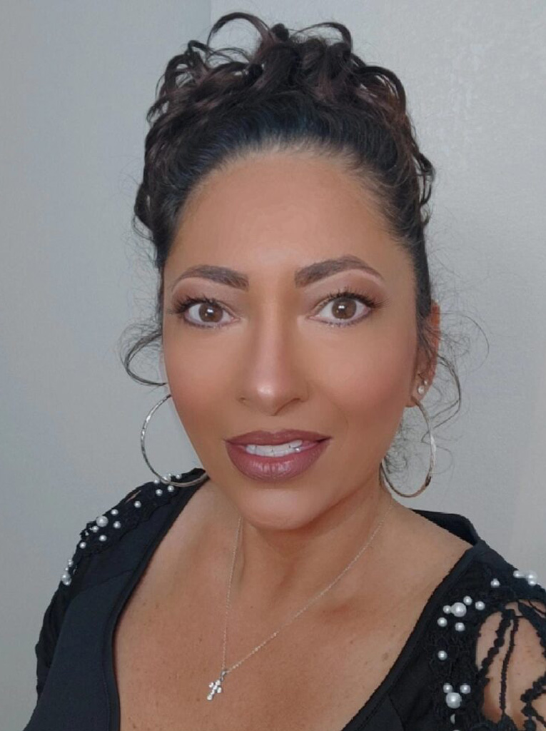 Woman with curly hair smiling at the camera, wearing a black top and hoop earrings.