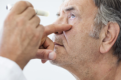 The image depicts a professional setting where a person is performing an eye examination on another individual using a device to measure visual acuity.