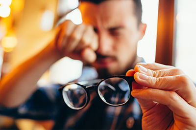 Man holding glasses with his left hand, looking downward with a thoughtful expression.