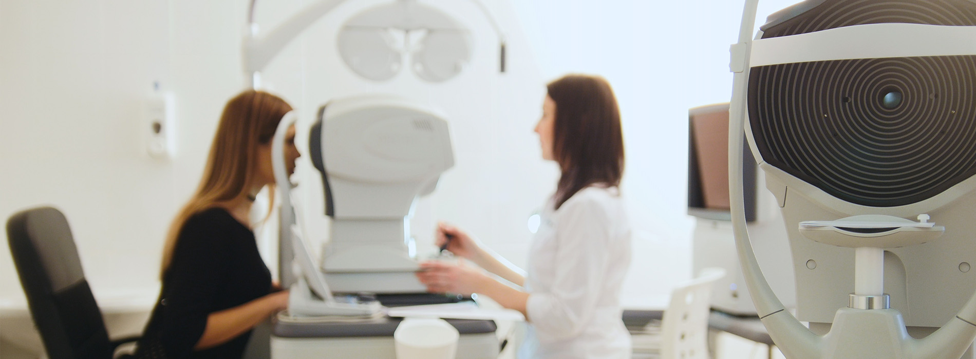 Two individuals seated at an optical equipment table with various instruments around them.