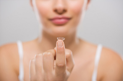 The image shows a close-up view of someone s hand holding a small object, possibly a contact lens, with a focus on the transparent material.