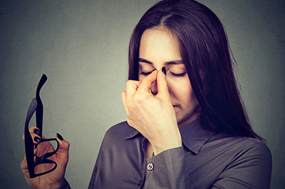 Woman with hand on face, holding glasses, appearing distressed or overwhelmed.