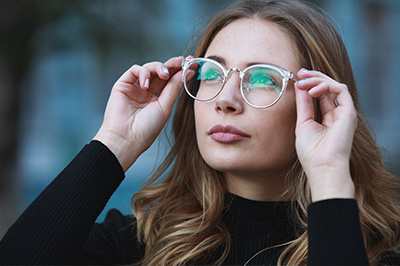 A woman wearing glasses and a black top, adjusting her eyewear while looking off to the side.