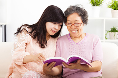 The image depicts two individuals, presumably an older adult and a younger person, sitting on a couch and looking at a book together.